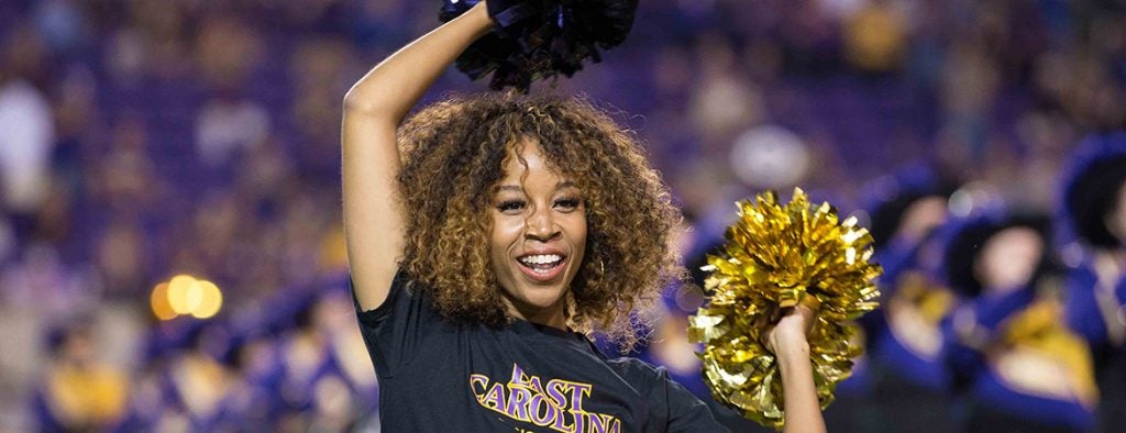 Closeup of a dance team member holding purple and gold pom poms above her head.