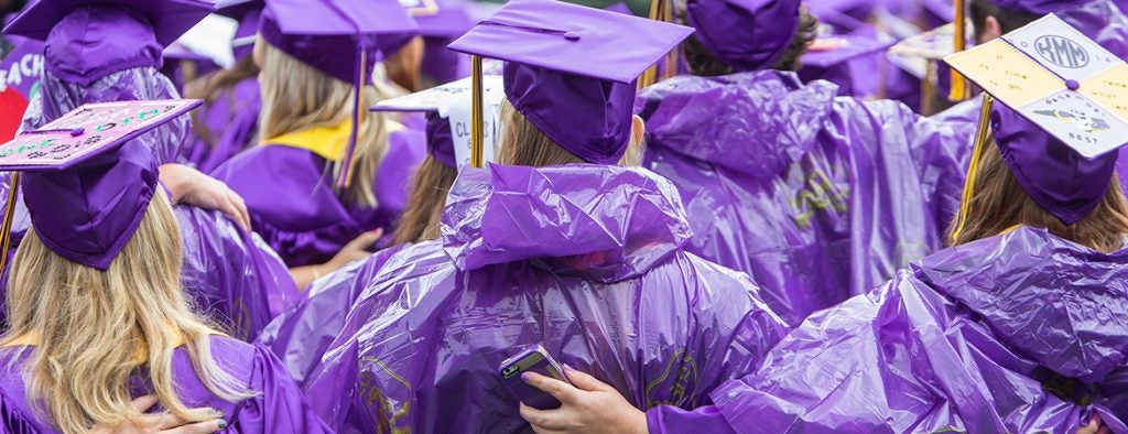 Graduates wearing purple graduation hats, gowns, and ponchos