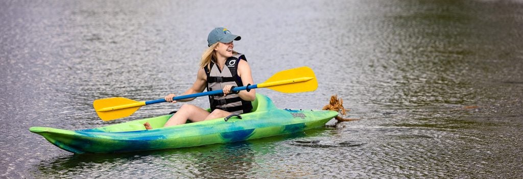 A female student in a kayak wearing a life vest and holding a paddle.