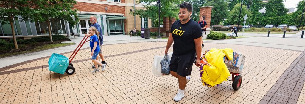 A student wearing an ECU t-shirt carries his belongings on a hand truck.