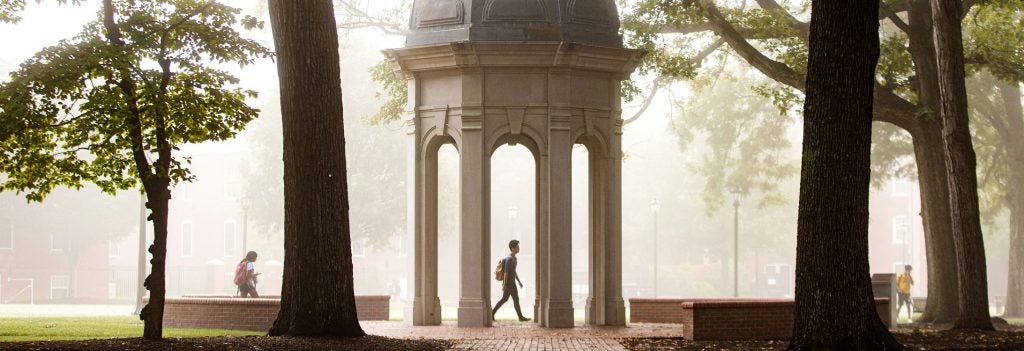 Student wearing a backpack walking past ECU cupola on a foggy day.