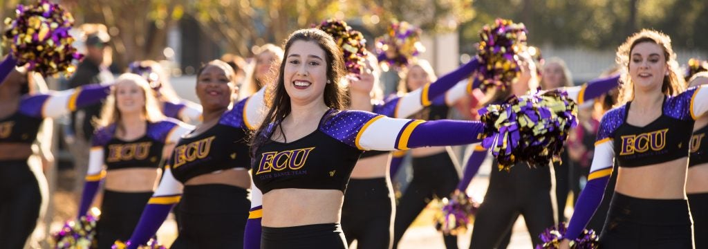 ECU dance team members wave purple and gold pom poms while dancing.