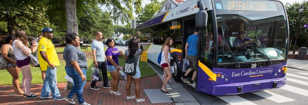 Group of people boarding an ECU Transit bus with a sign for Orientation on the front.