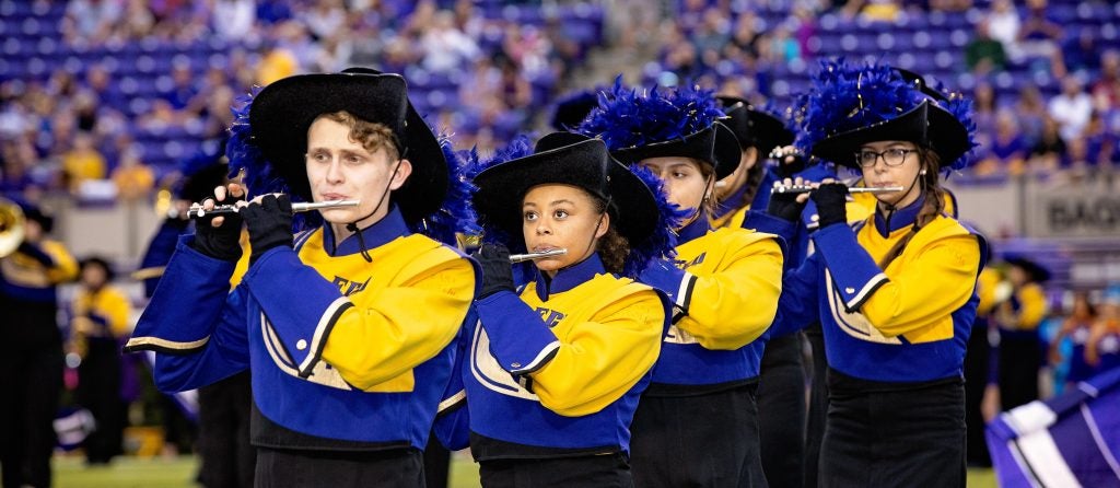 Members of the ECU marching band playing piccolos on the football field in their uniforms.