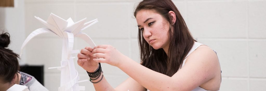 Female student constructs a sculpture from folded paper.